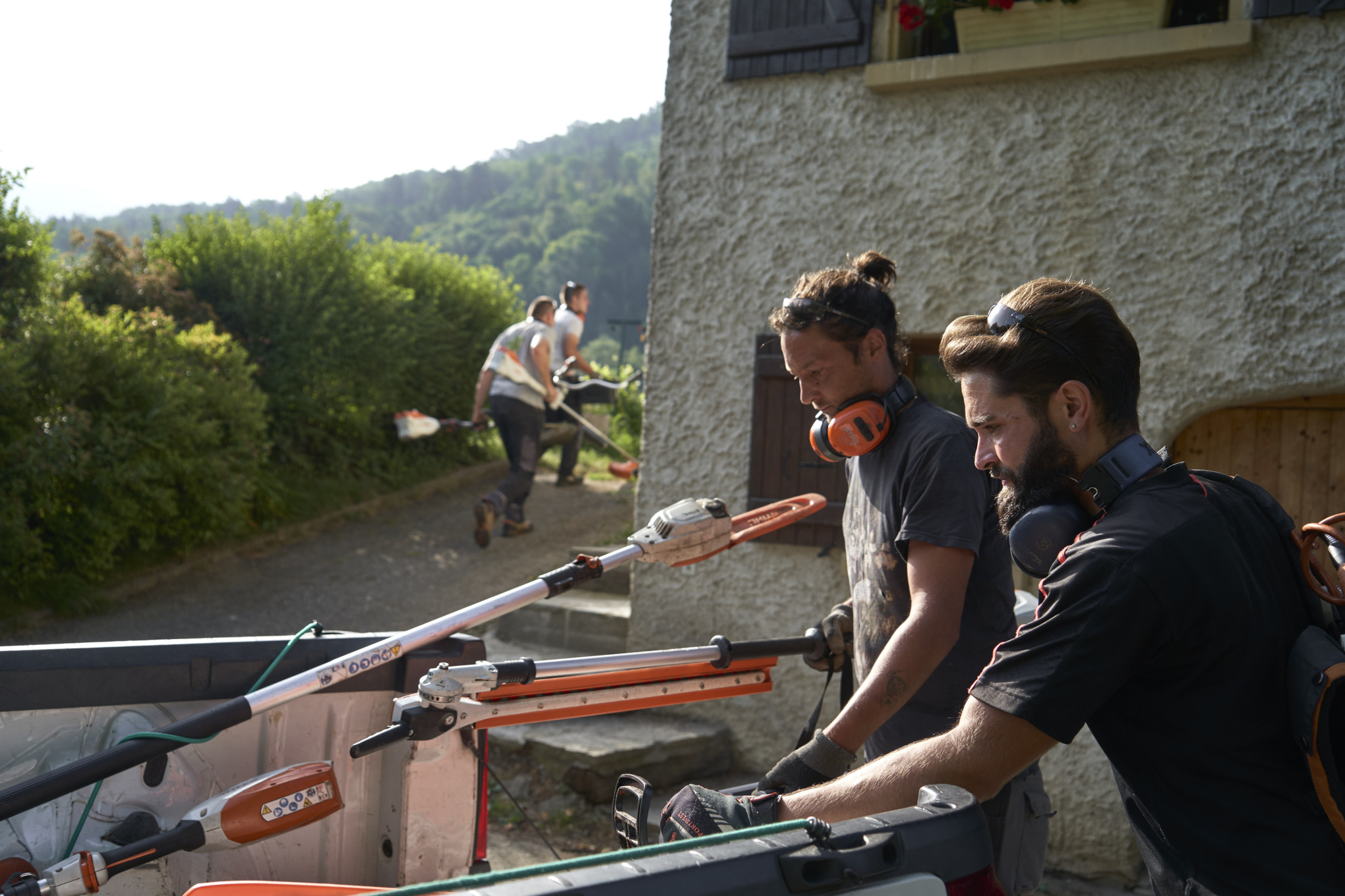 Dva pejzažna arhitekta istovaruju STIHL baterijske uređaje iz automobila, a ostali radnici se vide u pozadini 