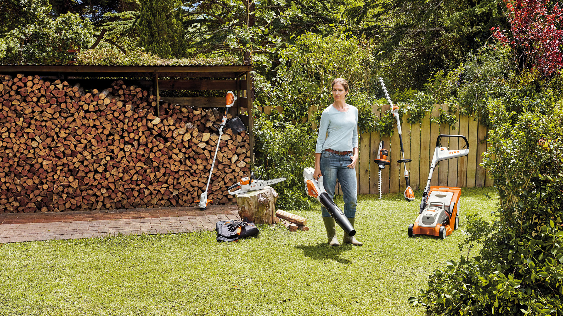 Ein Mann und eine Frau stehen in einem gepflegten Garten und betrachten lächelnd die Akku-Geräte aus dem STIHL AK-System