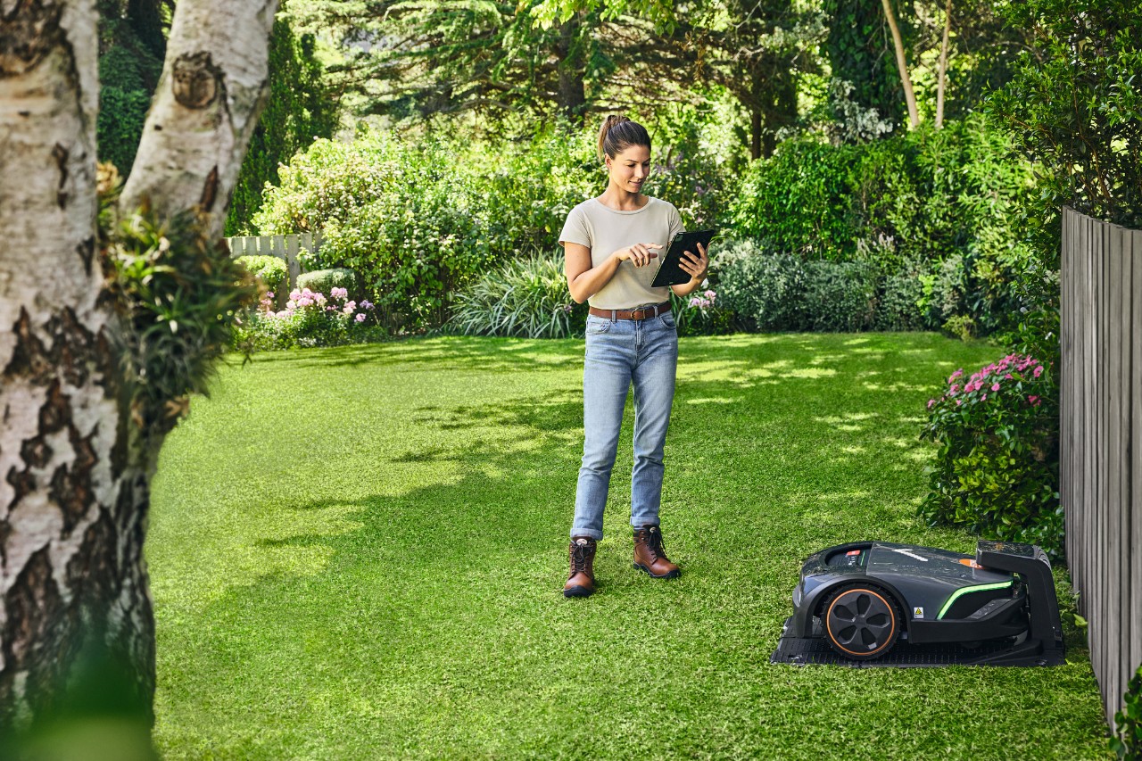 žena stoji na travnjaku pored IMOW kosačice sa  tabletom u rukama