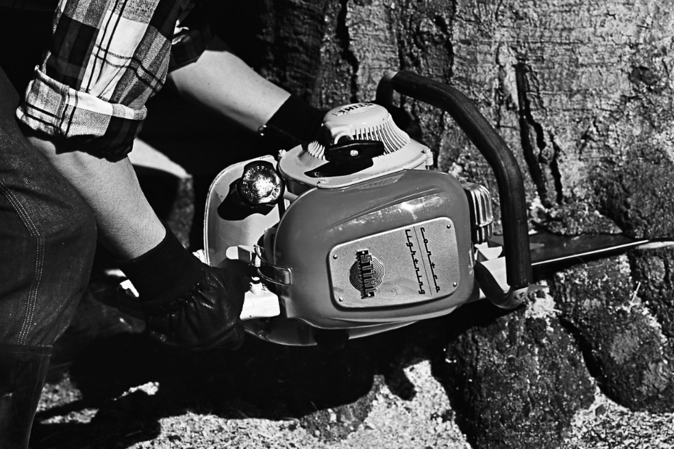 Stara crno-bela fotografija osobe u krupnom planu kako seče drvo motornom testerom STIHL Contra