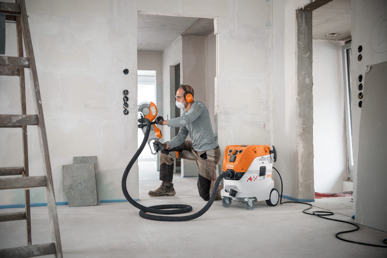 Muškarac koristi usisivač za mokro/suvo usisavanje STIHL SE 133 MM pri radu motornim sekačem STIHL TSA 230