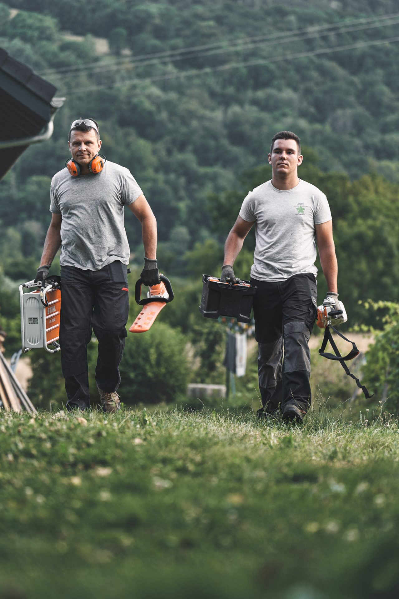 Dvojica profesionalaca idu preko travnjaka noseći STIHL baterijske uređaje u rukama