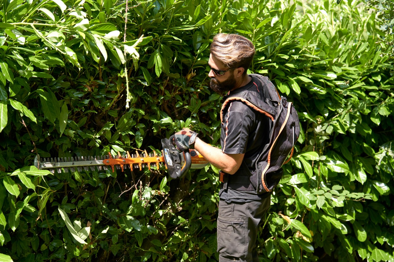 Profesionalac u zaštitnoj opremi orezuje živu ogradu STIHL baterijskim trimerom za živu ogradu