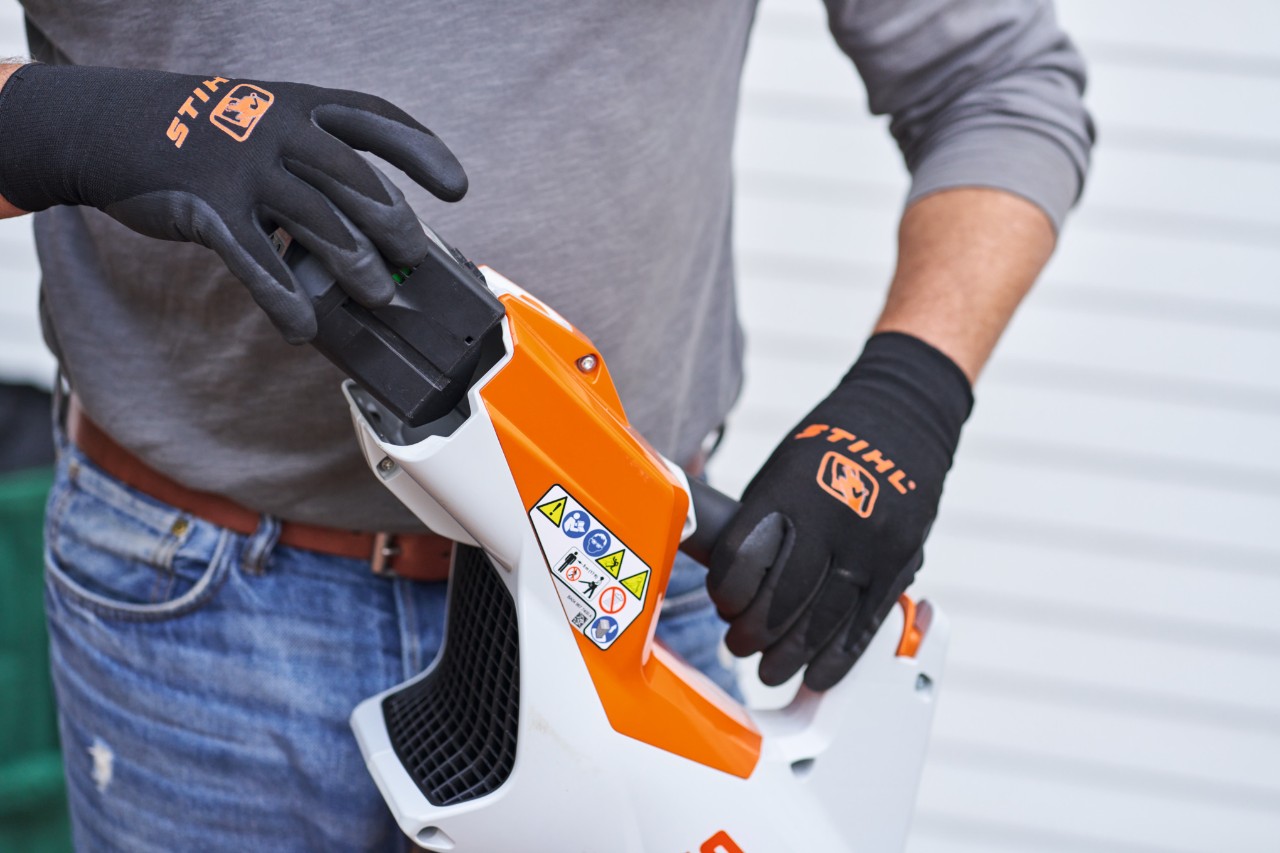 Osoba koja nosi crne STIHL rukavice vadi bateriju iz duvača