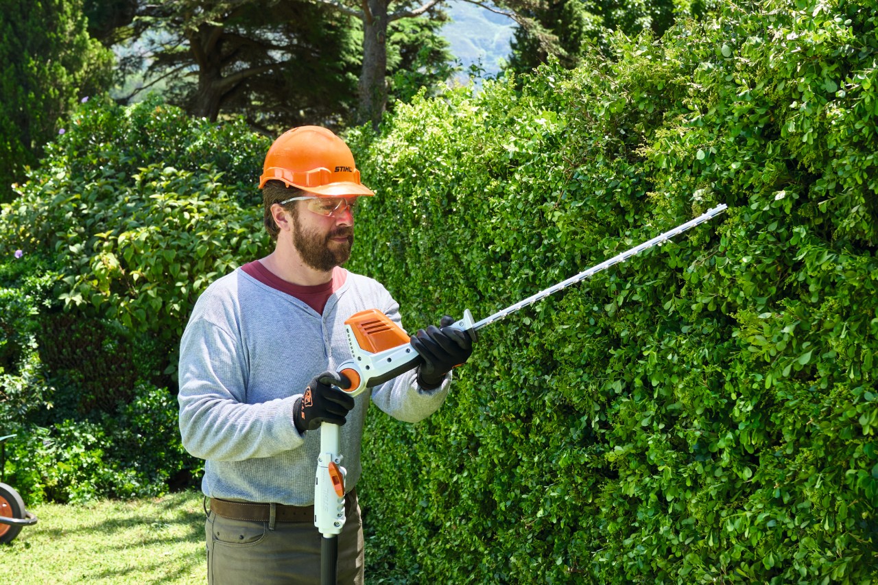 Čovek u zaštitnoj opremi orezuje visoku živu ogradu pomoću baterijskog trimera za živu ogradu STIHL HLA 56