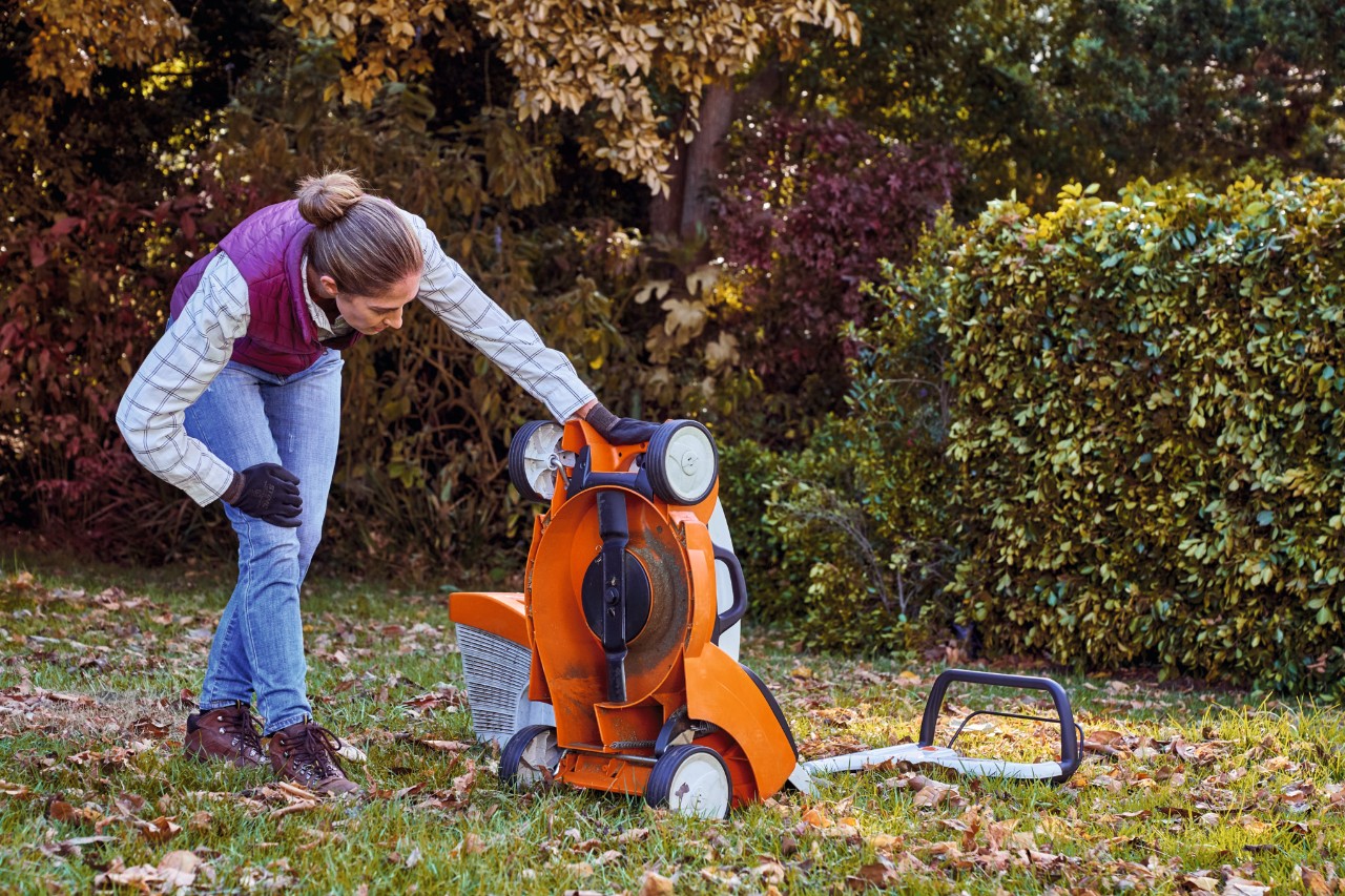 Žena pregleda donju stranu STIHL baterijske kosačice RMA 339 C u bašti tokom održavanja travnjaka u jesen 