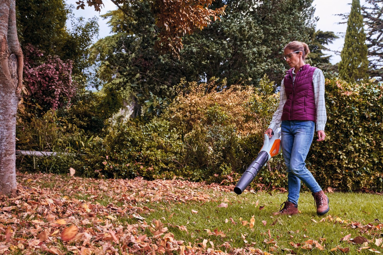 Žena duva lišče u jesen u bašti sa STIHL duvačem