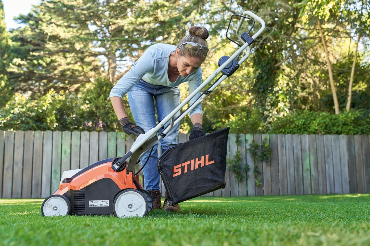Žena kači korpu za prikupljanje STIHL baterijskog prozračivača travnjaka RLA 240 sa zadnje strane mašine.