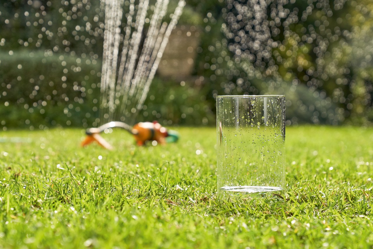 Voda se prikuplja u čaši iz prskalice u pozadini