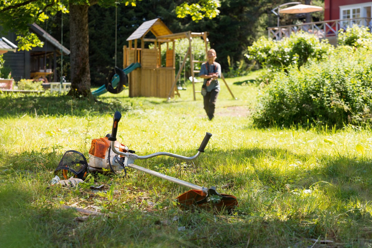 STIHL motorna kosa FS 240 leži u travi, u pozadini se čovek priprema za održavanje