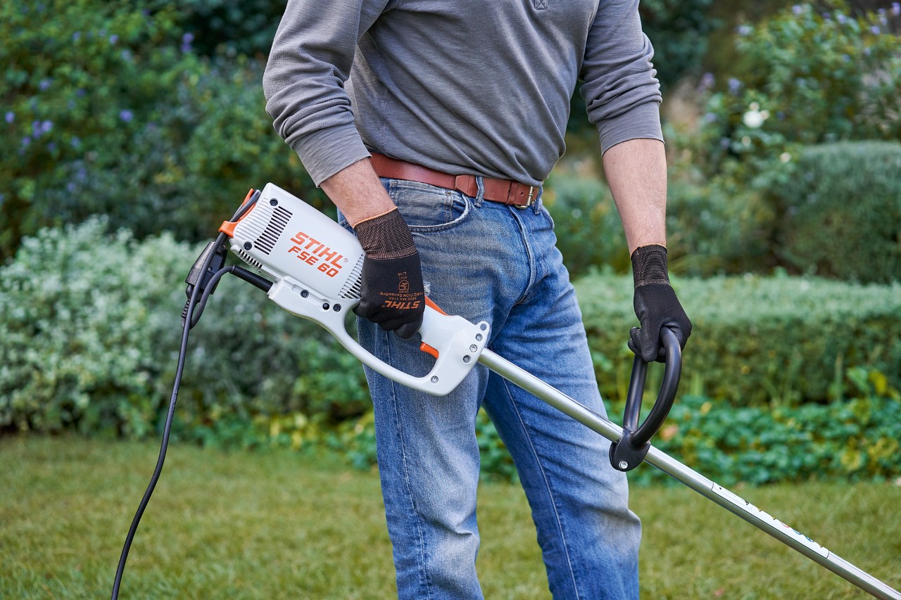 Čovek sa zaštitnim rukavicama drži električnu motornu kosu STIHL FSE 60 obema rukama