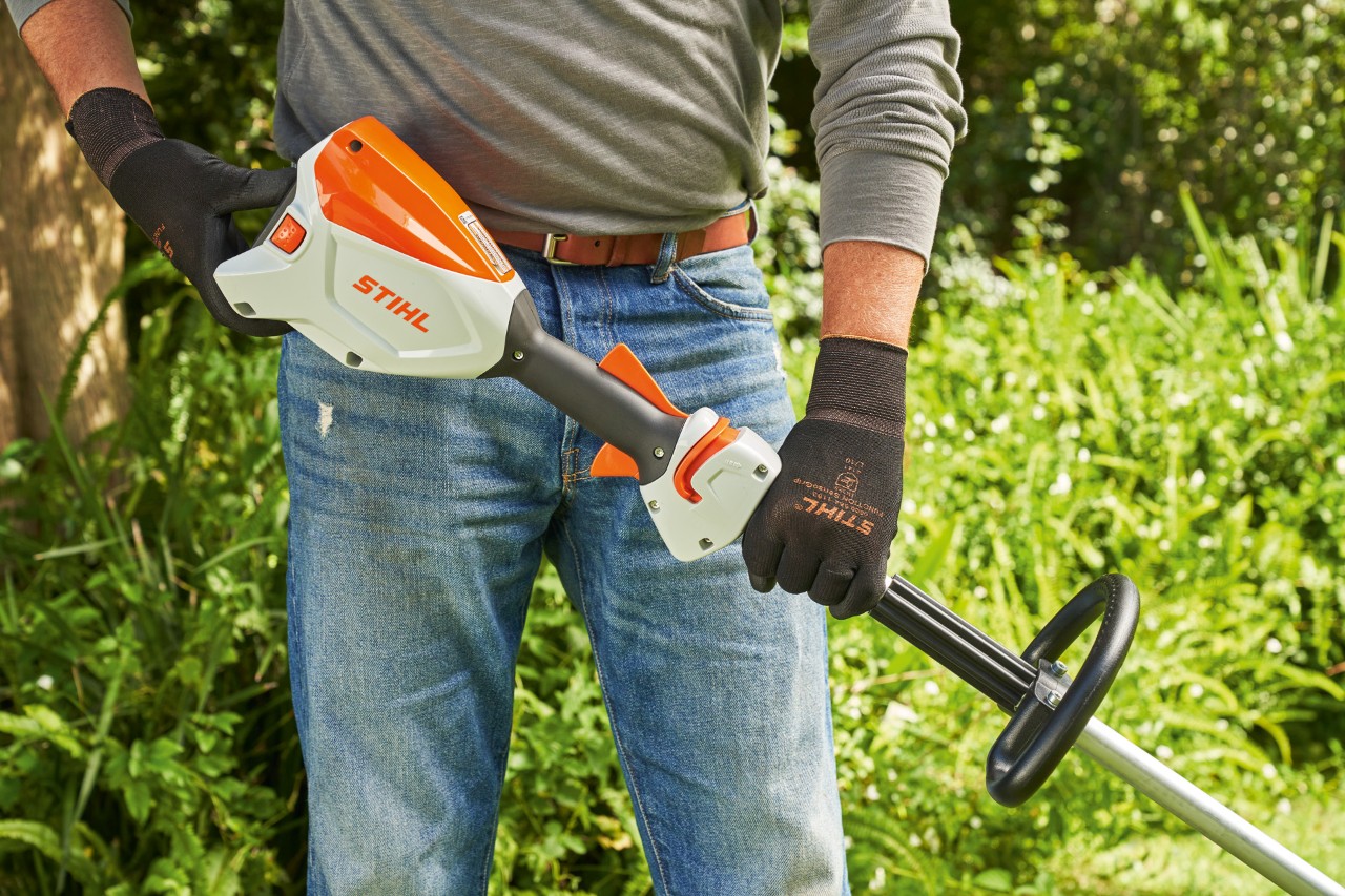 Čovek sa zaštitnim rukavicama proverava akumulator akumulatorske motorne kose STIHL FSA 60 kako bi pokrenuo motornu kosu