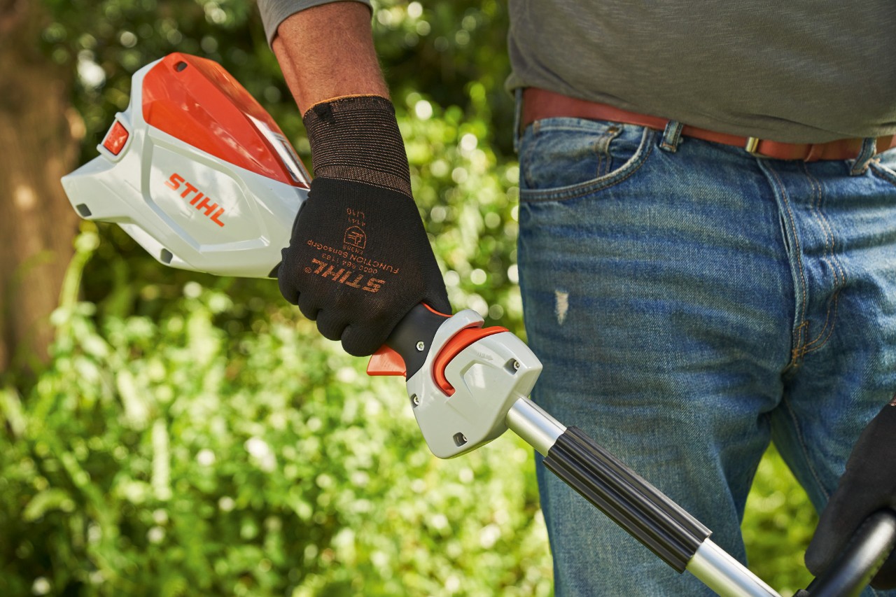 Čovek sa zaštitnim rukavicama pritiska blokadu ručice menjača akumulatorske motorne kose STIHL FSA 60 