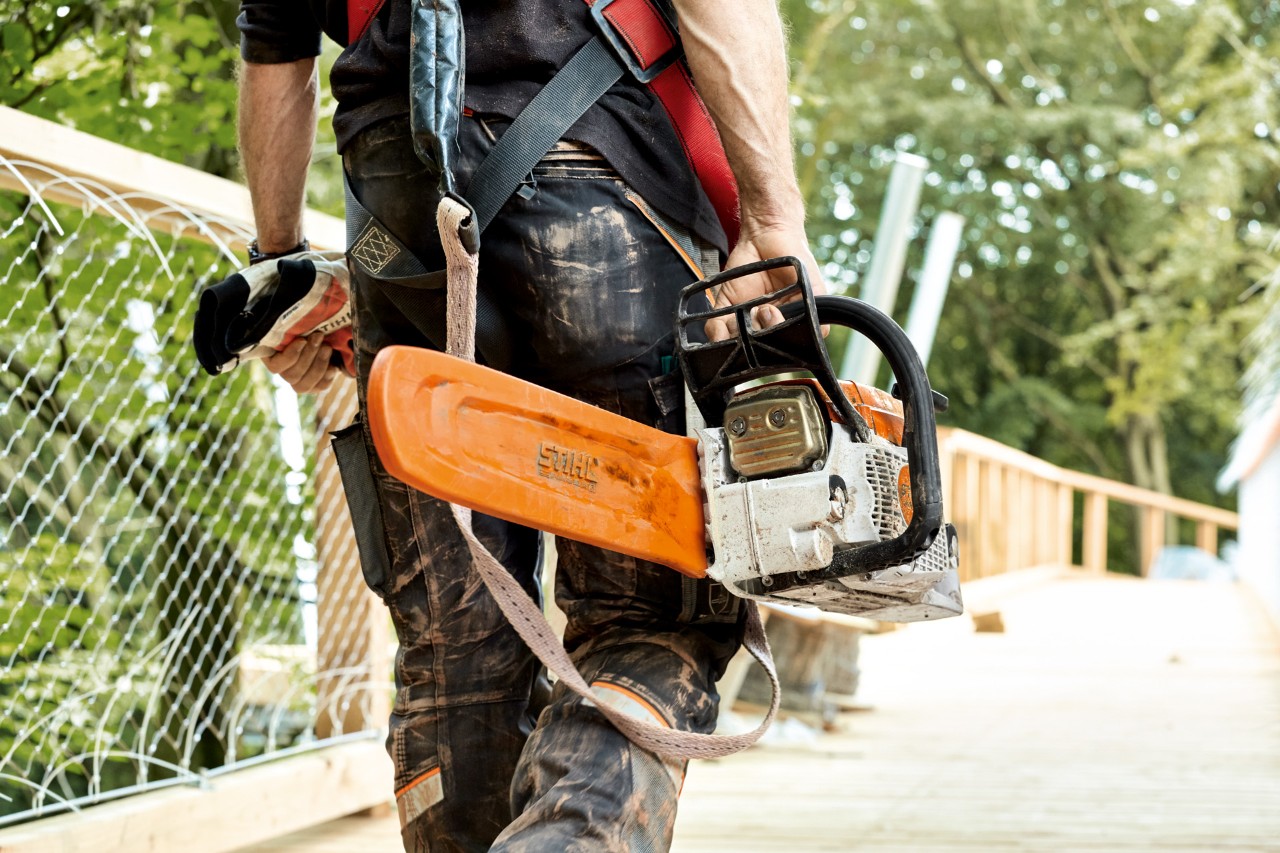 Čovek u zaštitnoj odeći nosi benzinsku motornu testeru STIHL MS 261 sa zaštitom za lanac.