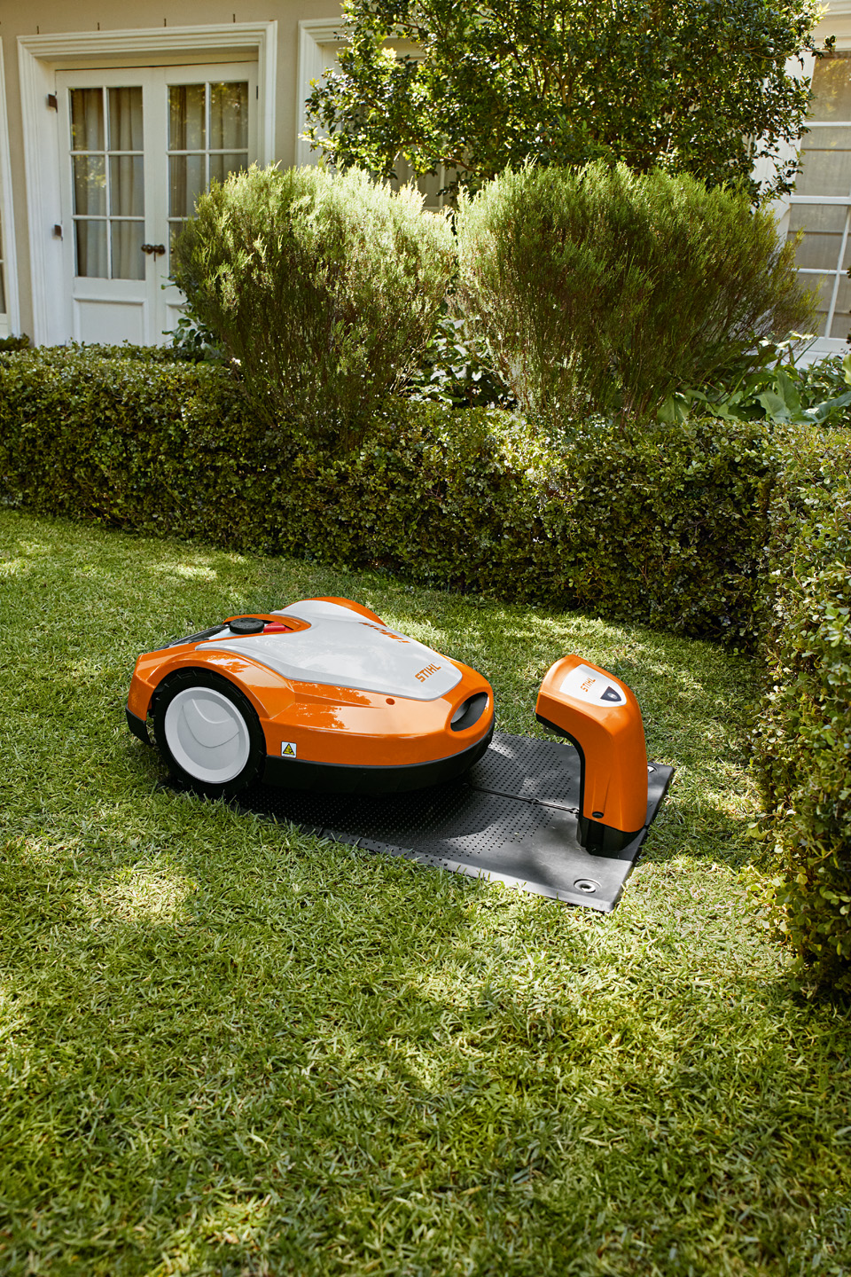 Robotska kosačica iMOW® RMI 632 proizvođača STIHL pored stanice za punjenje u dvorištu