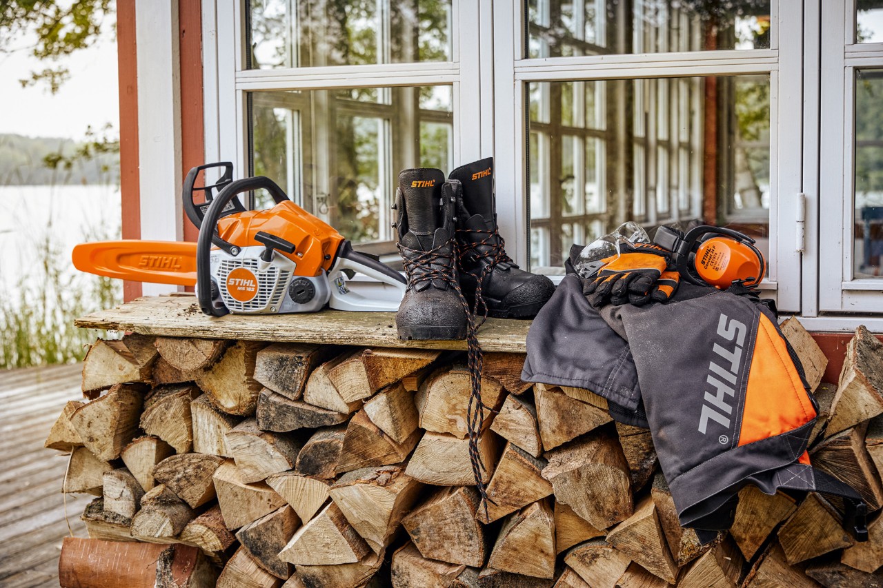 STIHL zaštitna odeća i MS 162 na polici iznad naslaganog drva za loženje