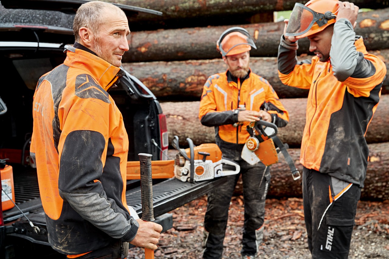 Tri muškarca u STIHL zaštitnoj odeći ispred naslaganih drva pripremaju se za rad sa STIHL lančanom testerom
